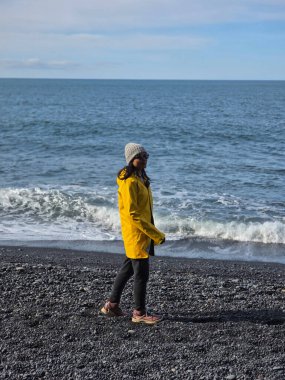 Reynisfjara Sahili İzlanda 'nın ikonik siyah kumları boyunca gezinen bir gezgin, nefes kesici kıyı manzaralarına dalmış. Dalgalar yavaşça çarpar açık mavi gökyüzünün altında gün doğarken.