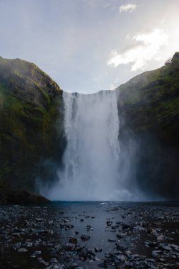 Skogafoss şelalesi, İzlanda 'daki yemyeşil yemyeşil bir havuza gök gürültüsüyle doluyor. Altın saat, bu nefes kesen doğa harikasına sıcak bir ışık saçıyor..