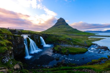 Kirkjufell Dağı, İzlanda 'da yemyeşil ve çağlayan şelaleler altında çarpıcı bir şekilde yükselir.