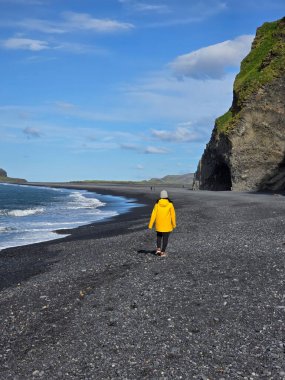 Asyalı bir kadın gezgin, İzlanda 'daki Reynisfjara Sahili' nin nefes kesici siyah kumsallarında yürüyor..