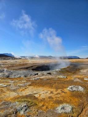 İzlanda 'daki geniş jeotermal arazide açık mavi gökyüzü altındaki jeotermal bacalardan canlı toprak tonları ve dalgalanan buhar bulunur. Doğanın çarpıcı bir temsili. Güç ve güzelliğin..