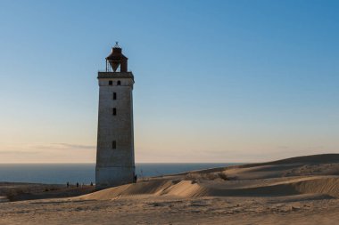 Kuzey Denizi 'nin akşam ışığında parlayan kayan kum tepelerinin önünde çarpıcı bir deniz feneri dimdik ayakta duruyor. Rubjerg Knude, Danimarka