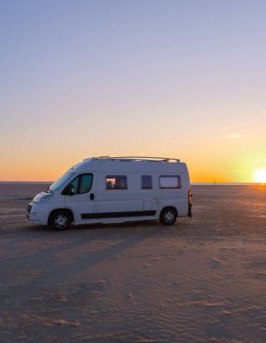Güneş batarken Danimarka 'nın kumlu kıyılarına park etmiş bir karavan gökyüzünde büyüleyici renkler bırakıyor ve suya yansıyor. Lakolk Strand, Romo Danimarka