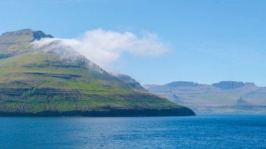 Faroe Adaları 'nın yemyeşil tepelerinin çarpıcı manzarası sakin mavi sulardan çarpıcı bir şekilde yükseliyor..