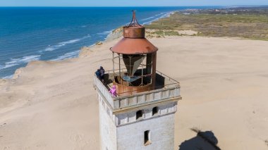 Ziyaretçiler Danimarka 'daki ikonik bir deniz fenerinin tepesinden nefes kesici manzaralara hayranlar. Bu kıyı mücevheri sonsuz plaj ve okyanusa eşsiz bir bakış açısı sunuyor, Rubjerg Knude, Kuzey Jutland 