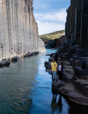 Ziyaretçiler, Studlagil Kanyonu 'nun dramatik uçurumlarını ve kristal berrak sularını keşfederler. Etrafı bazalt sütunlarla çevrilidir. İzlanda 'nın bu doğal harikasında unutulmaz bir macera bekliyor..
