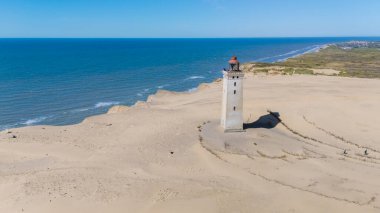 İkonik bir deniz feneri, Danimarka kıyıları boyunca uzanan el değmemiş kumsala bakar. Kıyıda hafif dalgalar var, Rubjerg Knude, Kuzey Jutland 
