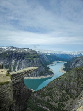 Norveç 'te Trolltunga' da manzaralı bir fiyortu çevreleyen yüksek uçurumlar ve yemyeşil vadiler, tek başına bir yürüyüşçü kenarda durur, bulutlu bir gökyüzünün altında nefes kesen manzarayı seyreder. Macera bekliyor..