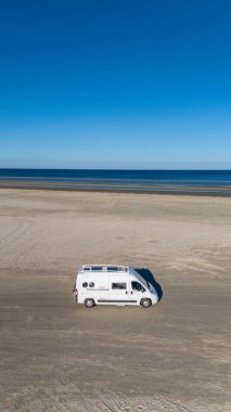 Romo Danimarka 'da sakin sular ve bulutsuz gökyüzü ile çevrili engin bir kumlu plajda park edilmiş bir karavan. Açık alan macera ve rahatlamaya davetiye çıkarır, doğa severler için mükemmeldir..