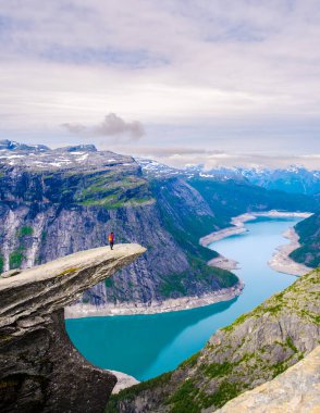 Yalnız bir yürüyüşçü dramatik bir uçurumun kenarında muzaffer bir şekilde durur, aşağıdaki ışıldayan turkuaz fiyorda bakar. Trolltunga, Norveç