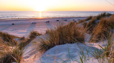 Sıcak güneş, Danimarka 'nın Vejers Strand plajındaki sakin plajın üzerinde batıyor ve kıyı şeridi boyunca altın renkler dökülüyor. Çimentoyla çevrelenmiş yumuşak kum tepeleri dingin bir atmosfer yaratır.