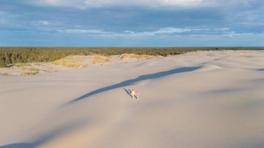 İki gezgin, sakin bir günbatımında Danimarka 'nın engin, açık renkli kum tepelerinde el ele yürürler. Sakin atmosfer, doğada keşif ve maceraya davetiye çıkarır. Rabjerg Mile Kumulları