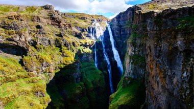 Yükselen kayalıklar İzlanda 'da, suların zarif bir şekilde yemyeşil bir vadiye yuvarlandığı bir Glymur Şelalesi' nin etrafını sarar. Kayanın ve yeşilliğin dramatik kontrastı doğanın güzelliğini vurgular..