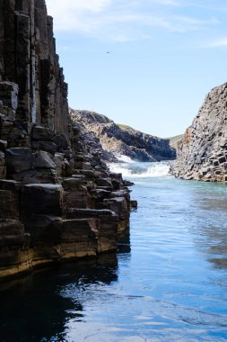 Yüksek bazalt sütunlar İzlanda 'daki Studlagil Kanyonu' nun derin mavi sularına sınır çizerek göz kamaştırıcı görüntüler yaratıyor. Güneş ışığı suyun üzerinde dans eder. Uzaktaki şelale gibi..