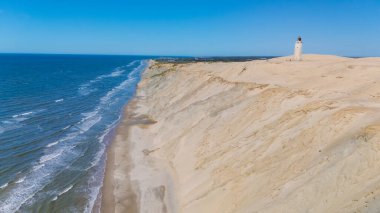 Rubjerg Knude deniz fenerinin çarpıcı sahil şeridini keşfedin. Kuzey Jutland Danimarka 'da altın kum tepelerinin canlı mavi okyanusla buluştuğu yerde. Uçurumların tepesinde gururla duran pitoresk bir deniz feneri