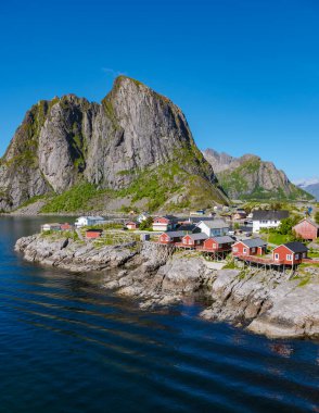 Parlak güneş ışığı, Lofoten Norveç 'teki büyüleyici kıyı köyünü aydınlatmakta, yüksek dağlar ve dingin sular arasında yer almaktadır. Canlı kırmızı evler güzel bir manzara yaratıyor, keşiflere davetiye çıkarıyor..