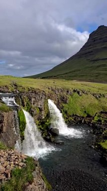 Şelaleler hareketli yeşillikler ve dramatik bir gökyüzü altında görkemli dağlarla çevrili sakin bir nehre dökülüyor. İzlanda 'nın bozulmamış el değmemiş doğasının saf güzelliğini hissedin. Kirkjufell İzlanda