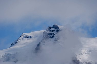 Svinafellsjokull Buzulu 'nun büyüleyici manzarası, yüksek tepelerin bulutlardan oluşan bir battaniyeyi delip geçtiği yer. Bu çarpıcı İzlanda manzarası, doğanın güzelliğini başka bir dünyada sergiliyor..