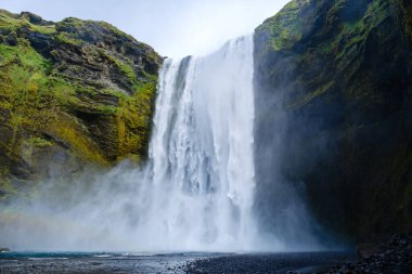 Skogafoss Şelalesi yeşil kayalıklarla çevrili nefes kesici bir dalış sergiliyor. Güneş ışığı, İzlanda 'nın doğal ortamında büyülü bir atmosfer yaratarak havada süzülüyor..