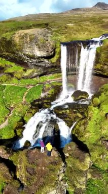 İzlanda 'daki Selvallafoss' a yolculuk, iki kaşif açık mavi gökyüzünün altında canlı yeşilliklerle çevrili çağlayan şelalelere hayran. Mükemmel bir doğa harikası karışımı..