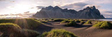 Stoksnes plajı, Vestrahorn İzlanda, geniş siyah kumsallar, arka planda dramatik dağlar belirdikçe yeşil otlaklarla tezat oluşturur..