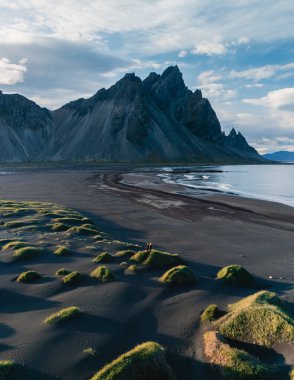 İzlanda 'daki Stoksnes' in siyah kumsalında yükselen Vestrahorn Dağı 'nın nefes kesici manzarası. Bereketli yeşil tufanlar, engebeli kayalıkların dramatik zeminine karşı çok güzel tezat oluşturuyor..