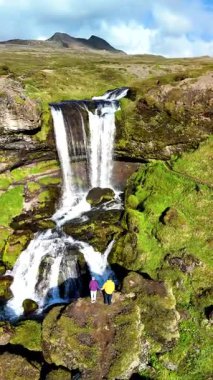 İzlanda 'nın dingin güzelliğini keşfedin. İki yürüyüşçü, yemyeşil bir alana kurulmuş görkemli bir şelaleye hayran. Bu nefes kesici konum İzlanda 'nın özünü yakalar eşsiz doğal harikalar.