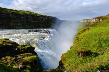Su İzlanda 'daki Gullfoss şelalesinin üzerinden güçlü bir şekilde akar ve güneş ışığıyla dans eden bir sis yaratır..