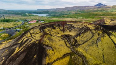 Grabrok kraterinin nefes kesici güzelliğini deneyimleyin, İzlanda 'da göze çarpan bir volkanik oluşum, yemyeşil ve dingin göllerle çevrili, canlı doğa renkleri ve dramatik arazi.