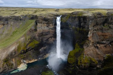 Haifoss şelalesi, yemyeşil tepeler ve kayalık kayalıklarla çevrili aşağıdaki kanyona çarpıcı bir şekilde dalıyor. Nefes kesici doğal güzellik, bulutlu bir günde İzlanda 'nın nefes kesici manzarasını sergiliyor..