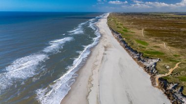 Danimarka kıyı şeridinin nefes kesici hava manzarası, kumlu kumsalın masmavi sularla buluşmasını gösteriyor. Yumuşak dalgalar kıyıya vuruyor, Lyngvig deniz feneri Hvide Sande Kuzey Jutland