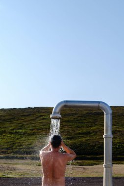 İzlanda 'daki doğal bir kaplıcadan ferahlatıcı bir duşun keyfini çıkarıyorum. Açık mavi gökyüzünün altındaki büyüleyici yeşil tepelerle çevrili. Rahatlamak ve doğayla bağ kurmak için mükemmel bir an. Krafla duşundaki adam.