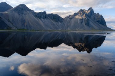 Vestrahorn dağı, sakin bir gökyüzüne çarpıcı bir şekilde yükselir. Yansıması İzlanda 'daki Stoksnes' in durgun sularında kusursuz bir şekilde yansımıştır.