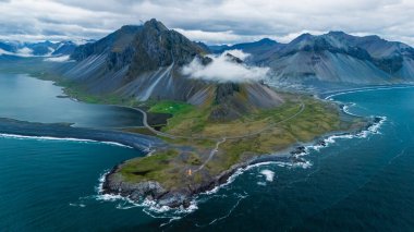 İzlanda kıyı şeridinin nefes kesen manzarası sisli, yemyeşil alanlar ve canlı mavi sularla kaplanmış yüksek dağları ortaya çıkarıyor. Bu çarpıcı manzara doğanın Hvalnes Doğa Koruma Alanı 'nı gösteriyor.