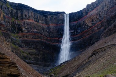İzlanda 'nın engebeli kayalıklarından gelen nefes kesici bir şelale dramatik kaya oluşumları ve canlı yeşilliklerle çevrili olarak İzlanda' nın vahşi doğasında şaşırtıcı bir doğa harikası yaratıyor..