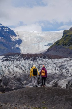 Maceraperest yürüyüşçüler, İzlanda 'da nefes kesici bir buz örtüsü olan Svinafellsjokull Buzulu' nun nefes kesici manzarasını izlerken engebeli arazide dururlar. Zengin dokular ve renkler doğanın güzelliğini gösteriyor.
