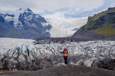 Svinafellsjokull Buzulu 'nun önünde, İzlanda' nın gökyüzünün altında çarpıcı buz oluşumlarıyla çevrili bir gezgin duruyor. Bu deneyim macera ve doğal güzelliğin özünü yakalar..