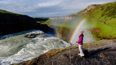 Gullfoss şelalesinin yanında duran bir gezgin, İzlanda 'daki sisli bir arazide gökkuşağı kavisleri gibi güçlü çağlayanı hayranlıkla seyrediyor.
