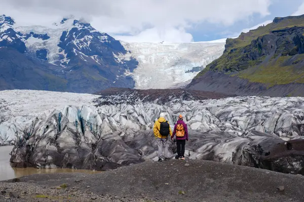 Svinafellsjokull Buzulu 'nun dramatik ve buzlu oluşumları arasında iki maceracı duruyor. Arka planda görkemli dağlar beliriyor, açık bir günde İzlanda 'nın engebeli güzelliğini gözler önüne seriyor..