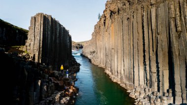 İzlanda 'daki nefes kesen Studlagil Kanyonu' nu araştırmak zümrüt sularının üzerinde yükselen muhteşem bazalt oluşumlarını ortaya çıkarıyor. İzlanda 'da tatilde olan birkaç erkek ve kadın.