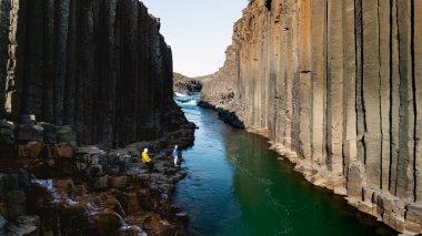 Ziyaretçiler, Studlagil Kanyonu 'nun yükselen bazalt sütunları ve canlı bir nehirle çevrili nefes kesici yüksekliklerini keşfediyorlar. İzlanda 'da tatilde olan birkaç erkek ve kadın.