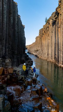 İki maceracı, Studlagil Kanyonu 'nun çarpıcı bazalt sütunlarında ve sakin sularında, İzlanda' da tatilde olan birkaç erkek ve kadın.