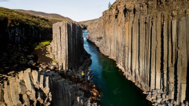 İzlanda 'daki Studlagil Kanyonu' nun turkuaz suları boyunca görkemli bazalt sütunlar yükseliyor. Bu çarpıcı doğa harikası yemyeşil manzaralar tarafından çerçevelenmiş, keşif ve maceraya davetiye çıkarıyor..