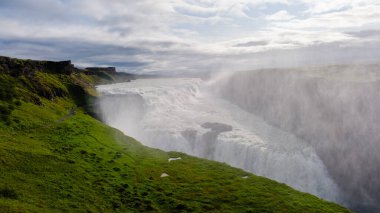 Gullfoss şelalesi zarif bir şekilde gürlüyor, yemyeşil tepeler ve dramatik uçurumlarla çevrili. Kükreyen şelaleden yükselen sis büyülü bir atmosfer yarattı..