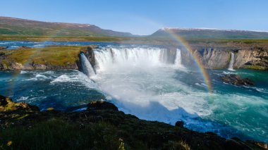 Godafoss şelalesi, İzlanda 'nın yemyeşil manzaraları arasında güçlü bir şelale oluşturarak çarpıcı bir manzara yaratır. Yukarıda canlı bir gökkuşağı beliriyor, İzlanda 'da güneşin doğuşundaki doğal güzelliği ekliyor.