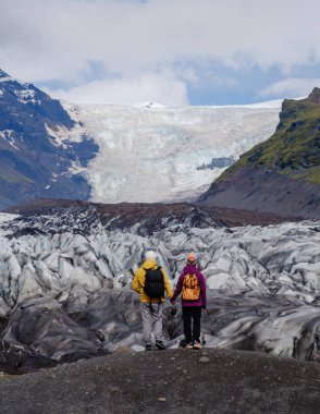 İki maceraperest yürüyüşçü el ele durup görkemli Svinafellsjokull Buzulu 'na bakıyorlar. Etrafı engebeli dağlar ve parlayan buzlarla çevrili bu yer doğa severler ve kaşifleri cezbediyor..