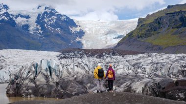 İki maceraperest engebeli arazide durup İzlanda 'daki şaşırtıcı Svinafellsjokull Buzulu' na bakıyorlar.