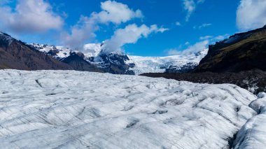 İzlanda 'daki Svinafellsjokull Buzulu' nun nefes kesici güzelliğini tecrübe edin. Parlak mavi gökyüzüne ve engebeli dağlara karşı yükselen buz oluşumları olağanüstü bir doğa harikası yaratıyor..