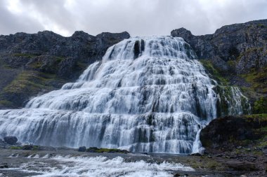 Bereketli yeşilliklerle çevrili İzlanda 'daki engebeli uçurumlardan çarpıcı bir şelale taşar. Dramatik manzara doğanın ham güzelliğini yansıtıyor Dynjandi şelalesi Batı Fiyort İzlanda