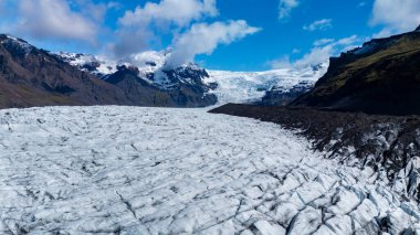 Yüksek buz oluşumları İzlanda 'daki Svinafellsjokull Buzulu boyunca uzanır, parlak mavi bir gökyüzünün altında. Bu nefes kesici buzullar İzlanda 'nın engebeli arazisinin ve buzulların güzelliğini gözler önüne seriyor..